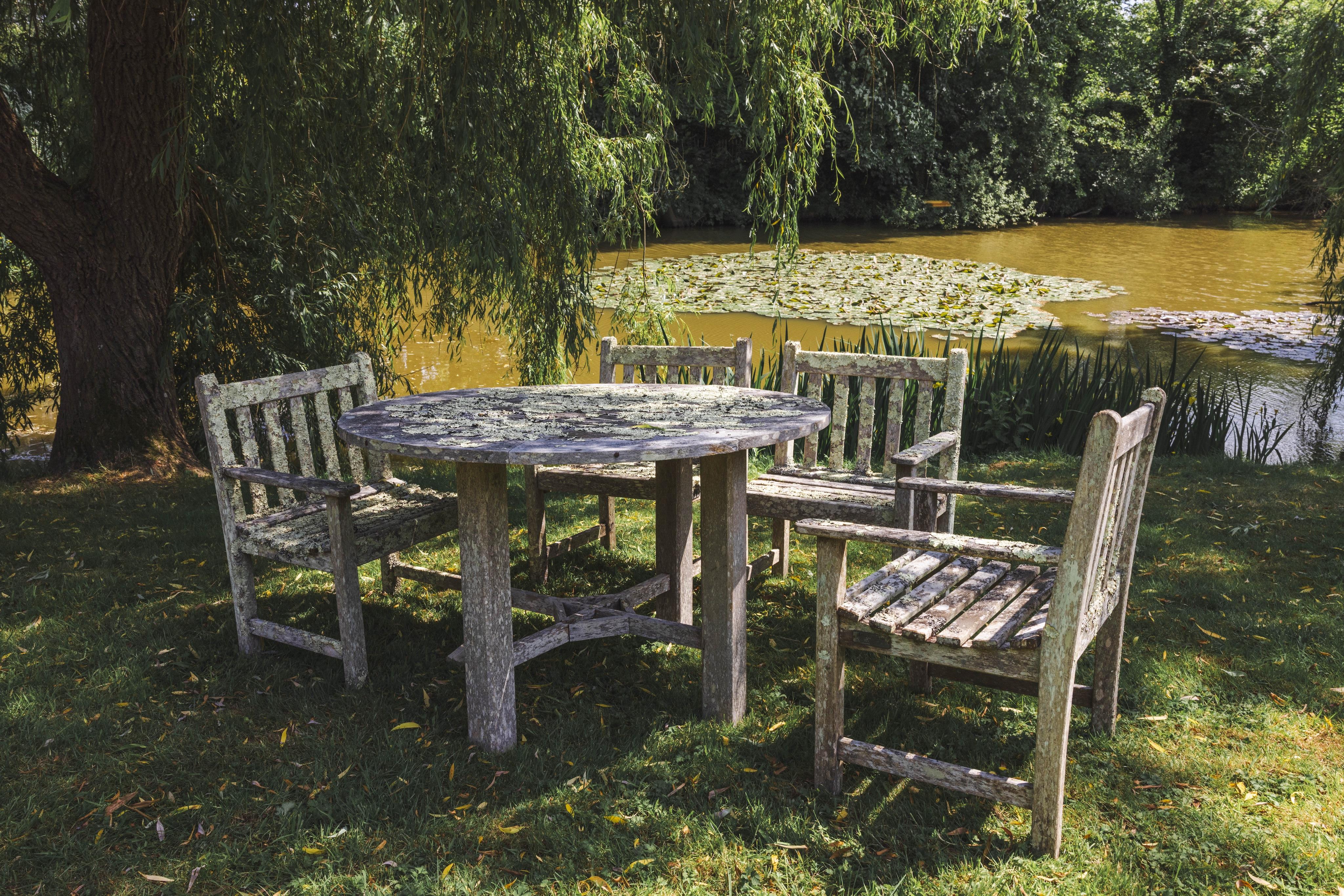 A weathered and lichen covered circular teak garden table, diameter 120cm, height 75cm and four armchairs